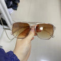 Sunglasses with brown lenses held by a hand against a neutral background