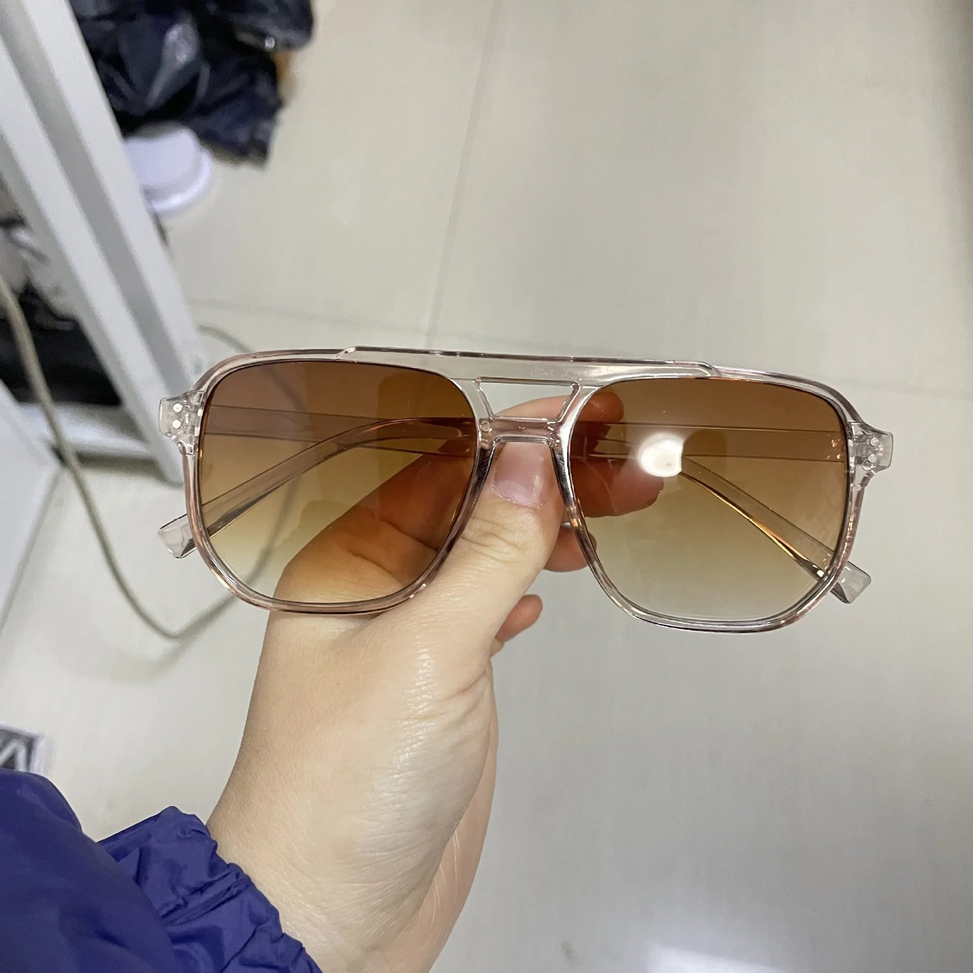 Sunglasses with brown lenses held by a hand against a neutral background